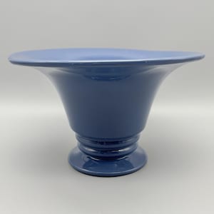 May include: A blue ceramic vase with a flared rim and a pedestal base. The vase has a smooth, matte finish and a classic, elegant shape. The vase is approximately 8 inches tall.