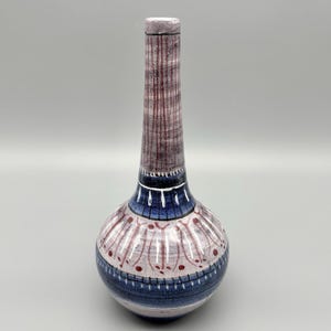 May include: A tall ceramic vase with a narrow neck and a rounded base. The surface features a hand-painted pattern of vertical brown lines on the neck, a band of deep blue, and a lower section with white petal-like shapes and red dots.
