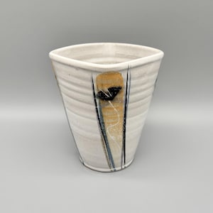 May include: A white ceramic vase with a square top and a slightly tapered body. The vase features a vertical design with a gold, black, and blue accent. The vase has a textured surface.