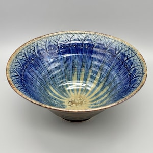 May include: A handmade ceramic bowl with a striking blue and yellow glaze. The bowl's interior features a radial pattern, with a textured rim. The bowl is a unique piece of art, perfect for serving or display.