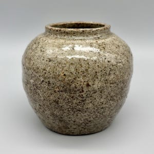 May include: A small, round, ceramic vase with a speckled brown and white glaze.