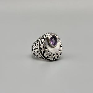 May include: A silver ring with an oval, purple gemstone set in a white, crescent-shaped inlay. The ring features an ornate, openwork design around the band and the gemstone setting. The ring is displayed on a gray background.
