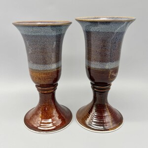 May include: Two ceramic vases with a flared top and pedestal base. The vases have a color gradient, transitioning from a dark brown base to a speckled brown middle section, and a blue-grey rim. The vases are approximately 10 inches tall.