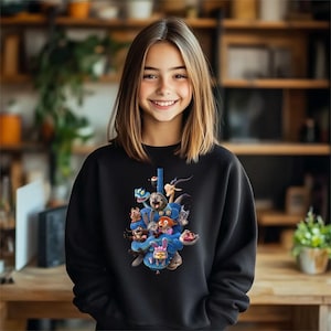 May include: Black sweatshirt featuring a colorful graphic of various cartoon characters wrapped around a blue snake. The design includes a variety of animals and creatures. The sweatshirt is made of a soft material.