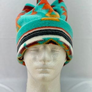 Puede incluir: Un gorro de forro polar turquesa con un patrón geométrico en tonos naranja, marrón y blanco. El gorro está doblado en la parte superior y tiene un ala ancha.