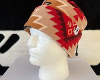 May include: A fleece beanie in tan, red, and brown with a geometric pattern. The hat is displayed on a white mannequin head. The beanie has a small tag on the side.