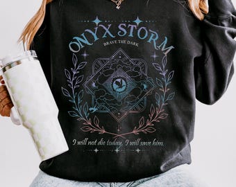 May include: Dark grey sweatshirt featuring the text "ONYX STORM" and "BRAVE THE DARK". The design includes a central graphic with a dragon and the phrase "I will not die today, I will save him."