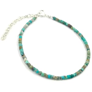 May include: A delicate turquoise bead bracelet with a silver-toned clasp and adjustable chain. The bracelet features small, square-cut turquoise beads in shades of blue, green, and brown. The bracelet is designed to be worn on the wrist.