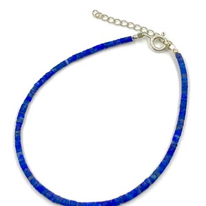 Puede incluir: Una delicada pulsera con pequeñas cuentas cuadradas de color azul oscuro. Las cuentas están ensartadas, formando una línea continua que se curva suavemente. La pulsera tiene un cierre plateado y una cadena ajustable.