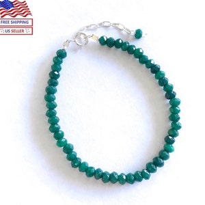 Puede incluir: Una pulsera delicada con cuentas facetadas de color verde esmeralda, ensartadas en una cadena y cierre plateados. Las cuentas son de tamaño uniforme y crean un bucle continuo. La pulsera se muestra sobre un fondo blanco.