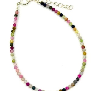Puede incluir: Una delicada pulsera con pequeñas cuentas facetadas en una variedad de colores, incluyendo rosa, verde y gris. Las cuentas están ensartadas en una cadena y cierre plateados. La pulsera es ajustable.