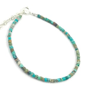 May include: A turquoise gemstone bracelet with a silver clasp. The bracelet is made of small, irregular shaped turquoise beads.