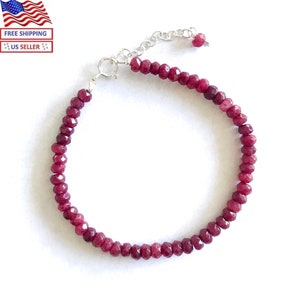 May include: A delicate bracelet featuring small, faceted, deep red gemstones strung together. The bracelet has a silver-colored clasp and adjustable chain. The gemstones are a rich, saturated color, and the bracelet is displayed against a white background.