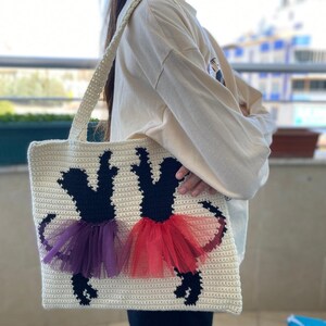 May include: A white crocheted tote bag with black silhouettes of two ballerinas wearing purple and red tutus.