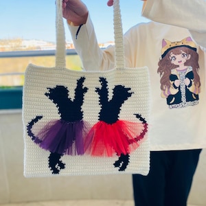 May include: A white crocheted tote bag with black silhouettes of two dancers wearing purple and red tulle tutus.
