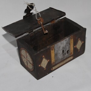 May include: A small wooden box with a hinged lid, decorated with metal accents and a keyhole. The box is open and the key is in the keyhole.
