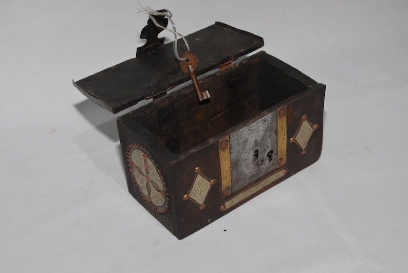 May include: A small wooden box with a hinged lid, decorated with metal accents and a keyhole. The box is open and the key is in the keyhole.