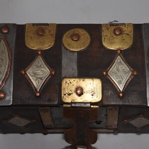 May include: A wooden box with a hinged lid, decorated with brass and silver accents. The box has a geometric design and is secured with a metal latch.