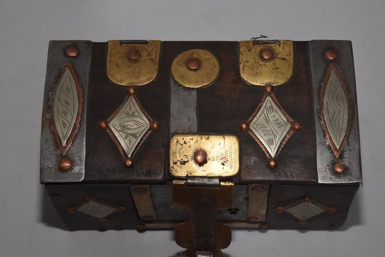 May include: A wooden box with a hinged lid, decorated with brass and silver accents. The box has a geometric design and is secured with a metal latch.