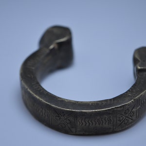 Könnte beinhalten: Ein silberfarbenes Metallarmband mit einem komplizierten geometrischen Muster. Das Armband ist offen und hat eine abgerundete Form.