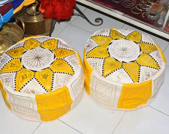 May include: Two yellow and white Moroccan poufs with intricate geometric patterns. The poufs are made of leather and have a traditional design.