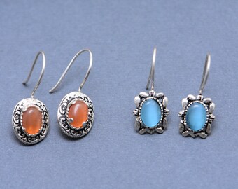 May include: A pair of silver earrings with orange oval-shaped stones and a pair of silver earrings with blue oval-shaped stones.