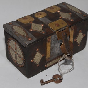 May include: A small, rectangular wooden box with a metal latch and key. The box is decorated with brass and silver accents, including a floral design on the side. The box is closed and the key is attached to the latch.