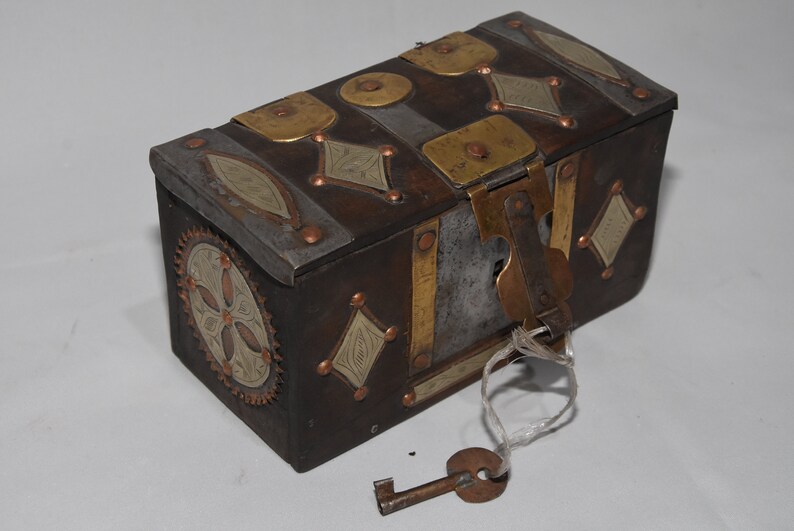 May include: A small, rectangular wooden box with a metal latch and key. The box is decorated with brass and silver accents, including a floral design on the side. The box is closed and the key is attached to the latch.