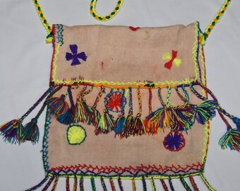 Puede incluir: Una bolsa de tela rosa con bordados coloridos y borlas. La bolsa tiene una correa de cordón amarillo y está decorada con flores y patrones geométricos.