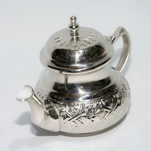 Puede incluir: Una tetera de plata con un diseño ornamentado y una tapa abovedada. La tetera tiene un pequeño pico y una asa.