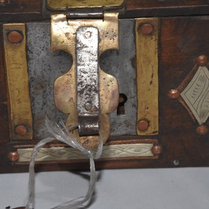 May include: A wooden box with a metal latch and keyhole. The box is decorated with brass and copper accents, and has a diamond-shaped design on the front.