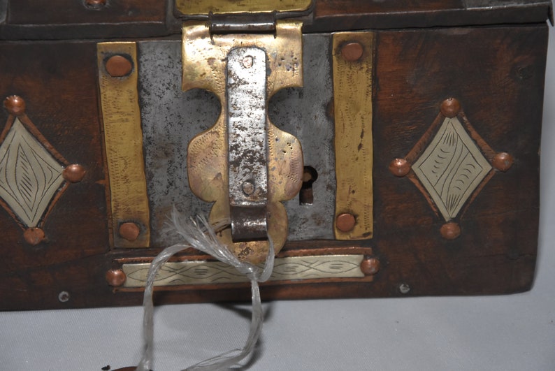 May include: A wooden box with a metal latch and keyhole. The box is decorated with brass and copper accents, and has a diamond-shaped design on the front.