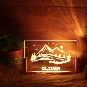 May include: A wooden night light with a mountain scene and the name "OLIVER" engraved on the front. The light is on and illuminating the scene.