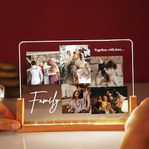 Puede incluir: Un expositor de fotos acrílico iluminado con base de madera. Muestra fotos familiares y la palabra "Family" en cursiva. También se ve la frase "Together, with love...". El expositor emite un brillo cálido y suave.