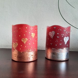 May include: Two red candle holders with gold and silver accents. The candle holders are decorated with hearts and dots.