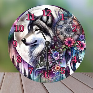 May include: Round wall clock featuring a wolf with black, white, and gray fur, set against a backdrop of a full moon and a dreamcatcher. The clock face has pink numerals and is adorned with flowers and feathers.