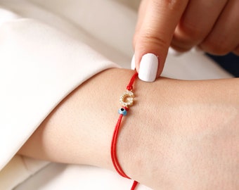 May include: Red string bracelet with a gold letter G charm and a blue evil eye bead.