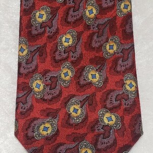 Puede incluir: Una corbata de seda roja con un patrón repetitivo de flores estilizadas en tonos dorados, azules y marrones.