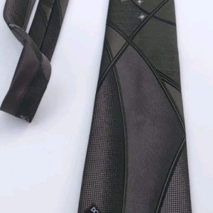 Könnte beinhalten: Eine dunkelgrüne und graue gemusterte Krawatte mit einem schwarzen Etikett, auf dem "DON LOPER BEVERLY HILLS" steht.