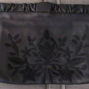 May include: Black leather clutch with a black floral embroidery design.