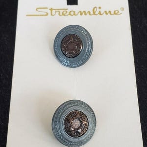 May include: Two gray buttons with a copper center design. The buttons have a raised, ornate border. The buttons are on a white card with the text "K9704 Streamline $2.50".