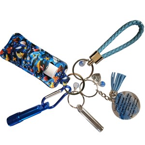 Puede incluir: Un juego de llaveros con una correa de muñeca trenzada azul, un mosquetón azul y una linterna azul. Incluye un soporte para bálsamo labial con un patrón azul con temática oceánica y un dije con el texto "Little Reminders".
