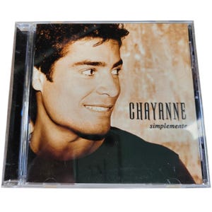 May include: A CD case with a portrait of Chayanne. The cover has a sepia-toned background with the artist's name in bold, black letters. The album title, "simplemente," is in a smaller font below the name.