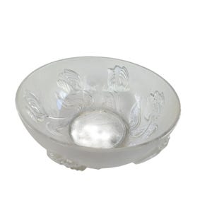 May include: A clear glass bowl with a frosted base and floral design. The bowl features embossed tulip-like flowers around the rim. The center of the bowl has a textured, circular pattern. The bowl is elevated on small, decorative feet.
