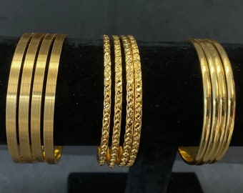 May include: Set of six gold-tone metal bangles. The bangles have different textures, including a smooth finish, a ribbed finish, and a textured finish.