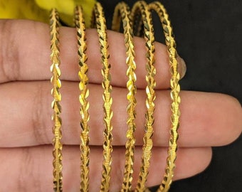 May include: A set of six gold-tone bangles with a textured, diamond-shaped pattern. The bangles are stacked on top of each other.