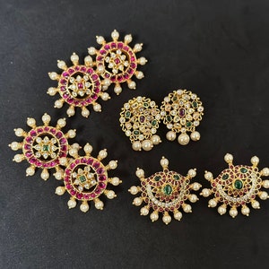 May include: A set of six gold earrings with intricate designs featuring pink, green, and white gemstones. The earrings are surrounded by a halo of small white pearls.