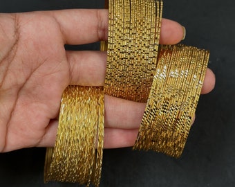 Op de afbeelding: Een set gouden metalen armbanden met een getextureerd, ruitvormig patroon. De armbanden zijn op elkaar gestapeld en worden in een hand gehouden.