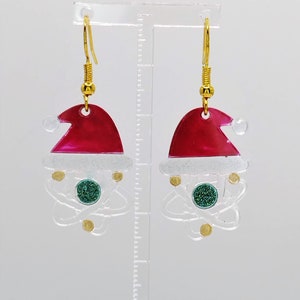 May include: A pair of dangle earrings featuring a red and white Santa hat with a green glitter atom charm.