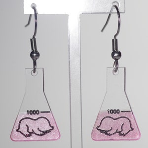 May include: A pair of pink and clear acrylic earrings shaped like beakers with a pink mole inside. The earrings have silver hooks.